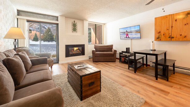 A living room with a fireplace, sofa, armchair, coffee table, TV, and wooden cabinet.