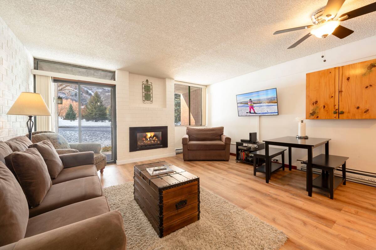 Ein Wohnzimmer mit Kamin, Sofa, Sessel, Couchtisch, Fernseher und Holzschrank.