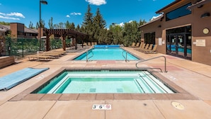 A pool area with two pools, lounge chairs, and a covered seating area.
