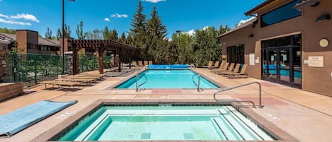 A pool area with two pools, lounge chairs, and a covered seating area.