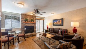 A living room with a stone fireplace, leather sofas, a glass coffee table, and a ceiling fan.