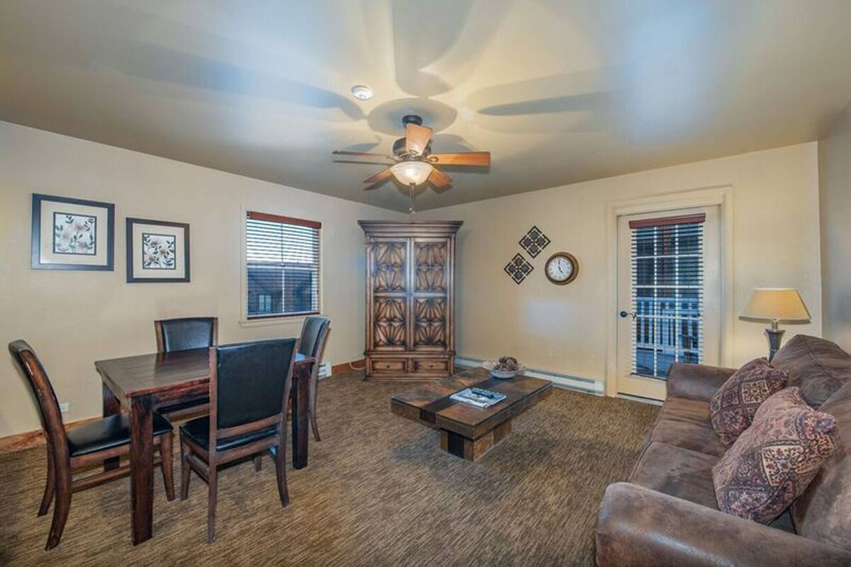 A living room with a dining table, chairs, a sofa, a coffee table, a ceiling fan, a cabinet, and a door with a window.
