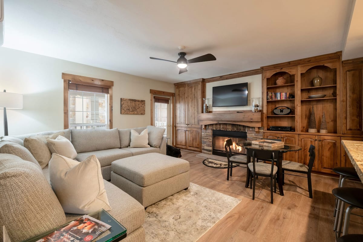 A modern living room with a sectional sofa, a fireplace, a television, and wooden cabinetry.