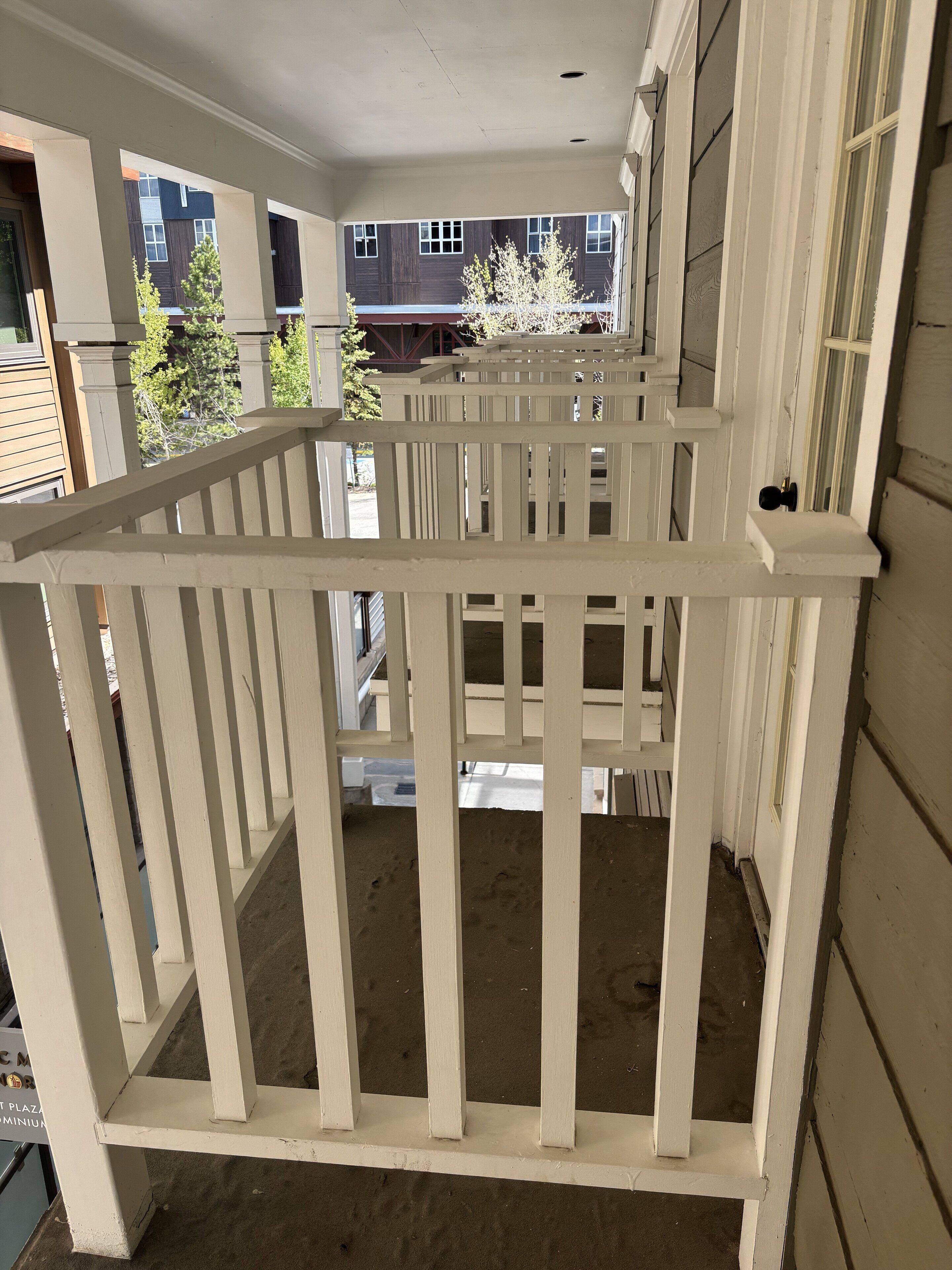 Ein weißer Holzbalkon mit Blick auf benachbarte Gebäude und Bäume.