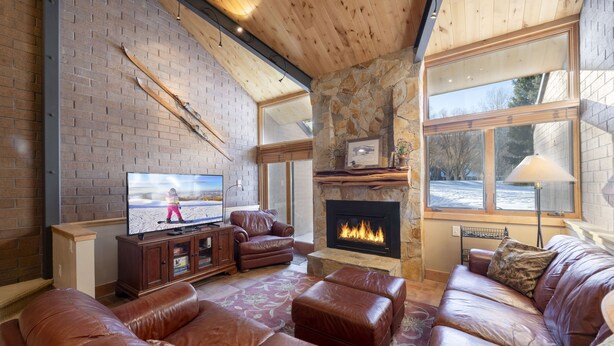 A cozy living room with a fireplace, leather sofas, a television, and a stone wall. - Park Avenue Upgraded 2 Bedroom Condominiums (Park City)