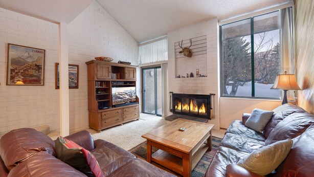 A cozy living room with a fireplace, leather sofas, a coffee table, and a bookshelf. - Park Avenue 3 Bedroom Condominiums (Park City)