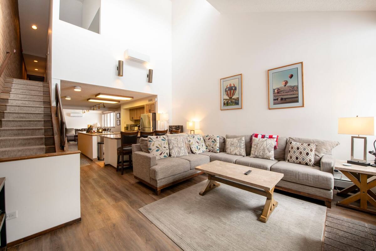 A spacious living area with a sofa set, a coffee table, and a staircase leading to an upper level.