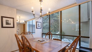 A dining area with a wooden table and chairs, large windows, and a chandelier. - Park Avenue 3 Bedroom Condominiums (Park City)