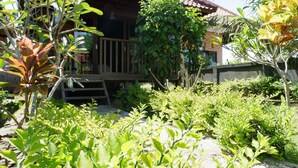 Una terraza de madera que conduce a una casa con techo de tejas, rodeada de exuberante vegetación y diversas plantas.