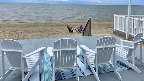 En strandutsikt med ett trädäck, vita Adirondack-stolar och ett räcke med utsikt över havet.