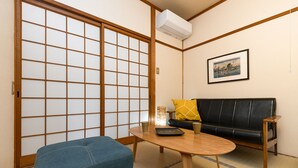 A traditional Japanese room with tatami flooring, a sliding shoji screen, a black leather sofa, a wooden table, and a small tatami mat bench. - Dongurian (Kyoto)