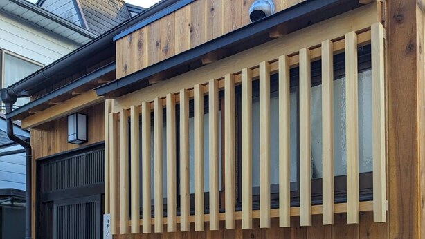 A wooden exterior wall with a black door and a vertical wooden slat design. - Dongurian (Kyoto)