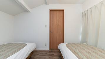 A room with two single beds, a wooden door, and a light switch on the wall.