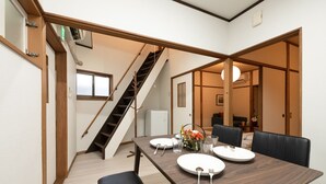 A dining area with a wooden table set for two, a staircase, and a view of a living area. - Dongurian (Kyoto)
