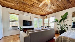 Een moderne woonkamer met een houten plafond, een grote bank, een flatscreen televisie en een potplant.
