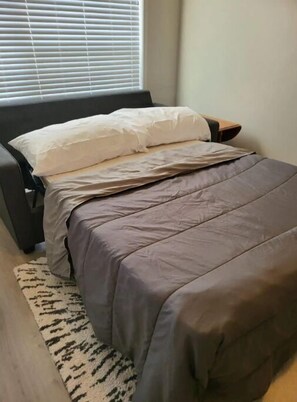 Cozy retreat with a comfortable bed, patterned rug, and a window with blinds.