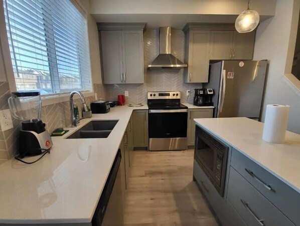 Features a sleek kitchen with stainless steel appliances, refrigerator, oven, microwave, sink, and countertop.