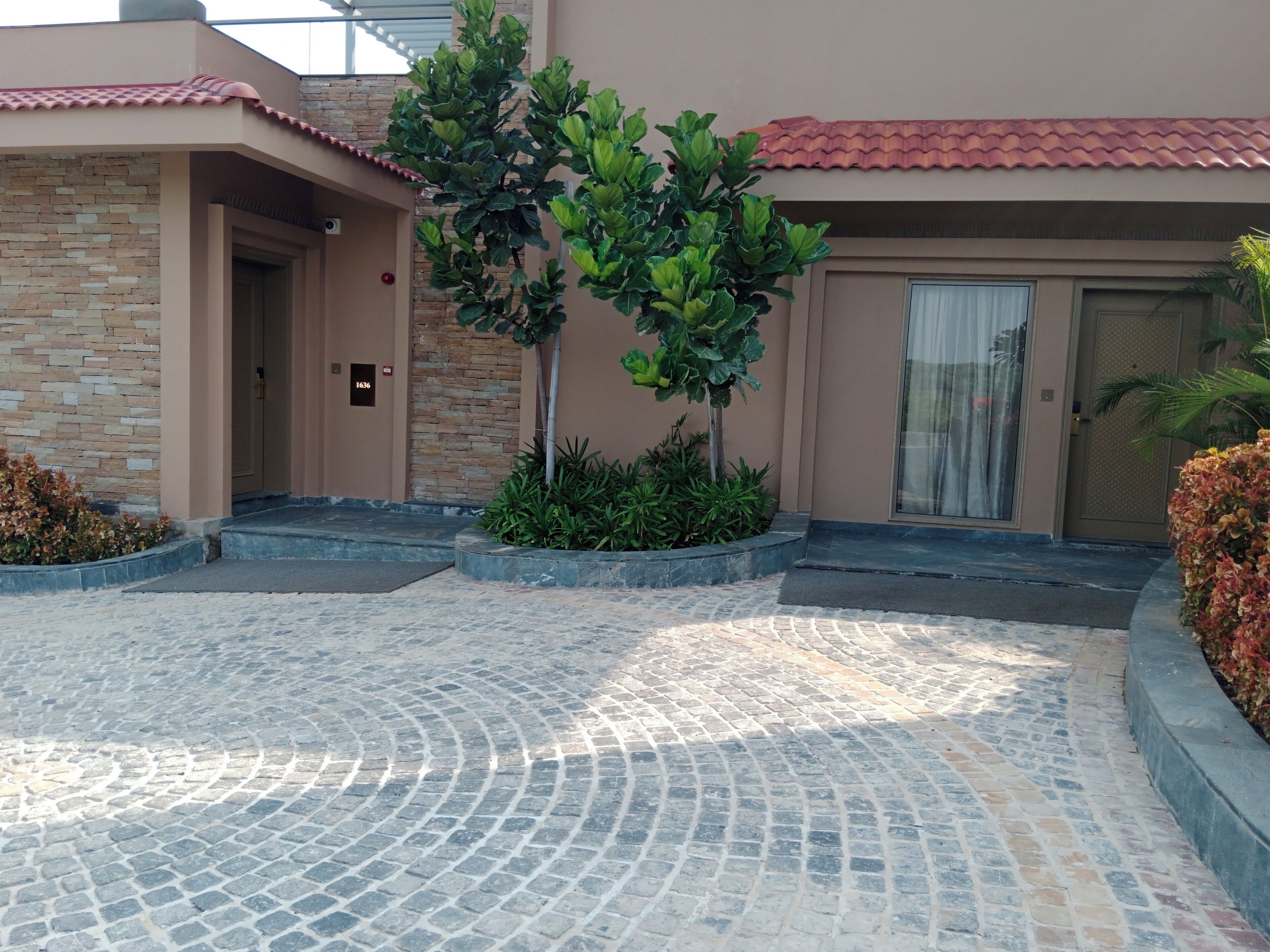 A building entrance with a stone facade, a tiled roof, and a paved courtyard with a curved pattern.