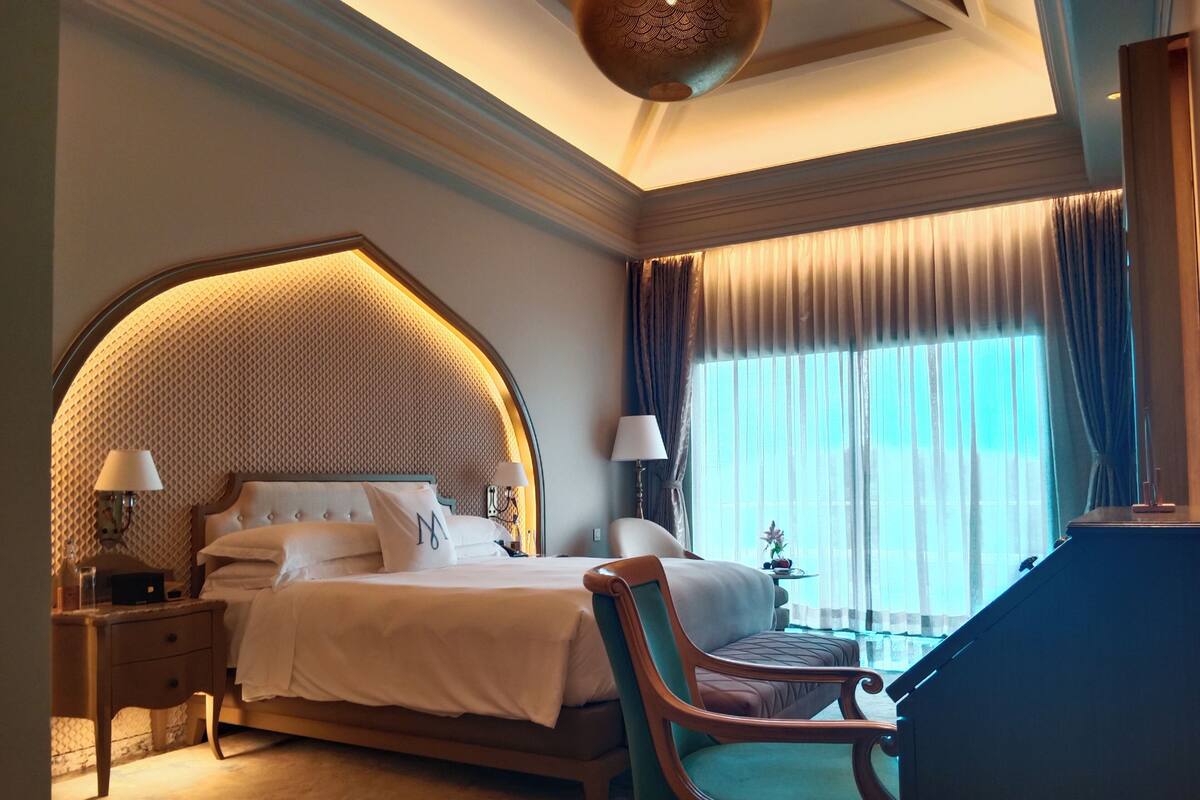 A hotel room with a large bed, two bedside tables with lamps, a wooden chair, and a desk.