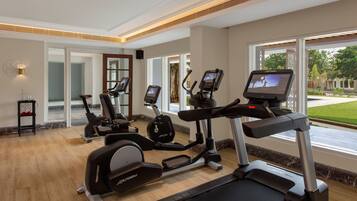 A gym with treadmills and elliptical machines, large windows, and a wooden floor.