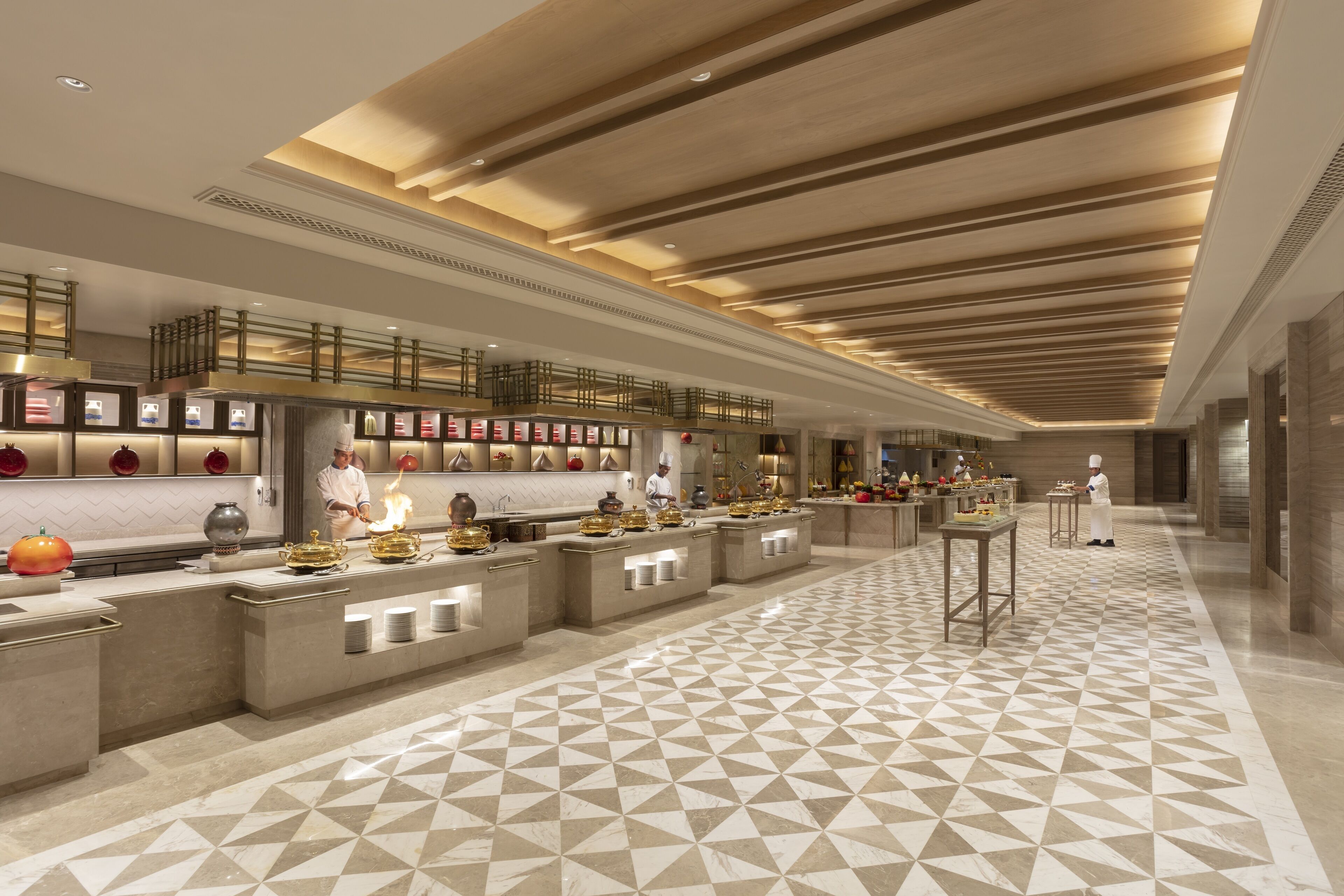 A modern kitchen with a geometric tile floor, stainless steel appliances, and a long counter with a chef preparing food.