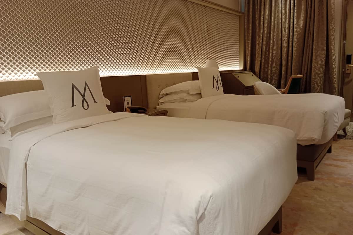 A hotel room with two beds, each with a pillow marked with a large 'M'.
