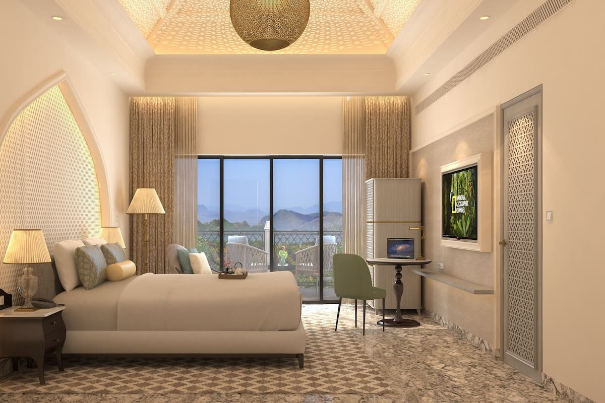 A hotel room with a large bed, two bedside lamps, a desk with a computer, a TV, and a view of the mountains.