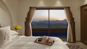 A hotel room with a large bed, a tray with breakfast items, and a view of mountains at sunset. - Mementos By ITC Hotels Ekaaya Udaipur (Udaipur)