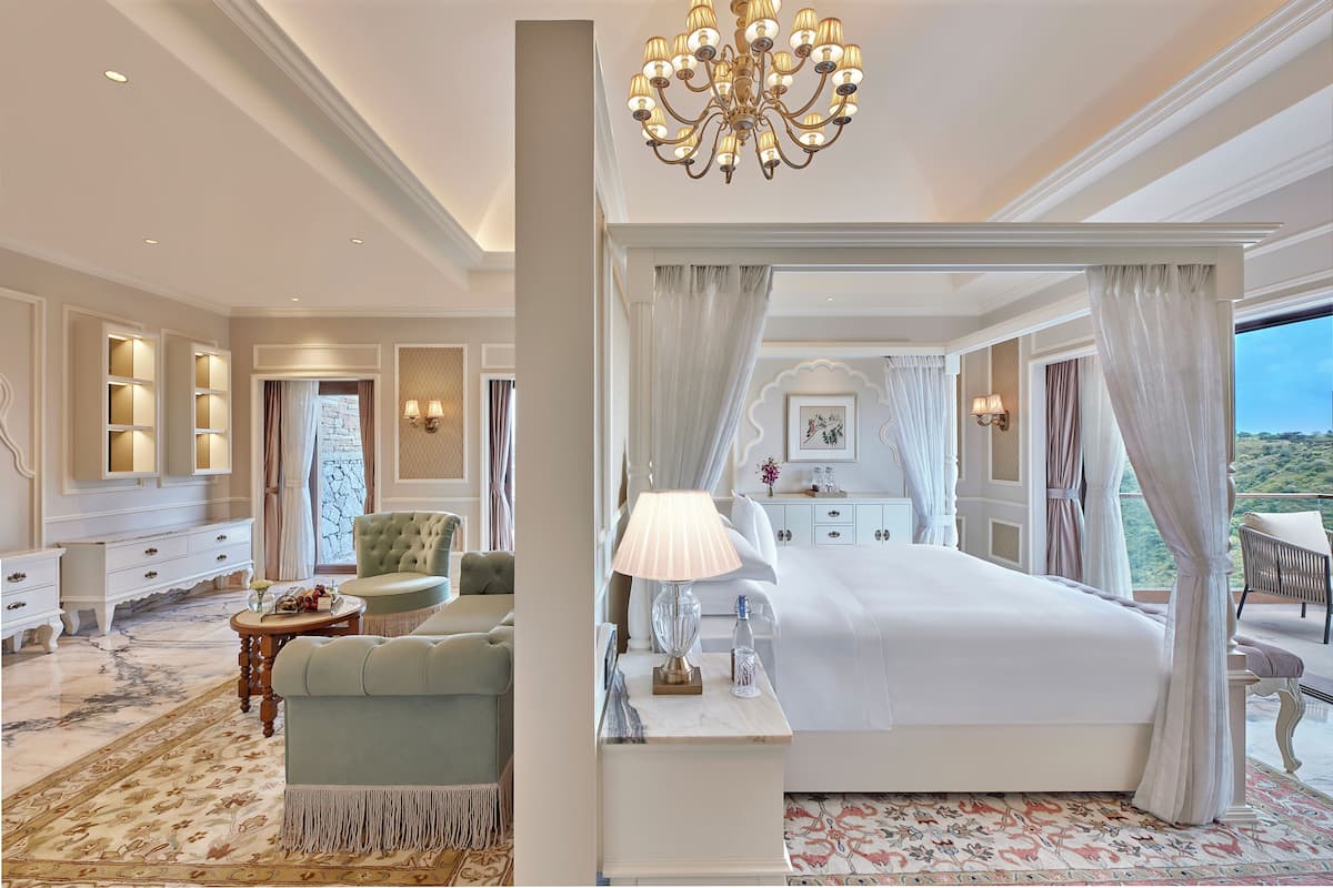 A luxurious bedroom with a four-poster bed, a chandelier, and a view of the landscape.