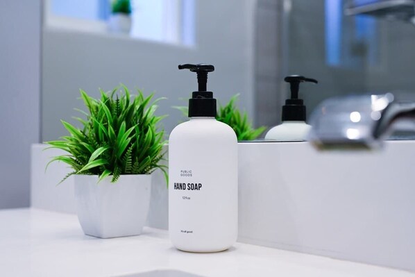 Une salle de bain avec un lavabo blanc, un distributeur de savon liquide et une plante en pot.