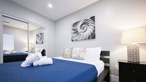 A modern hotel room with a large bed, a mirror, a wall art piece, a bedside table, and a lamp. - Stylish Central San Jose 3B2B w/crib Free Parking (San Jose)