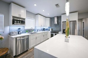 Une cuisine moderne avec des meubles blancs, des appareils électroménagers en acier inoxydable et un îlot central.