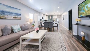 A modern living room with a sofa, coffee table, and a painting of a beach scene. - Stylish Central San Jose 3B2B w/crib Free Parking (San Jose)