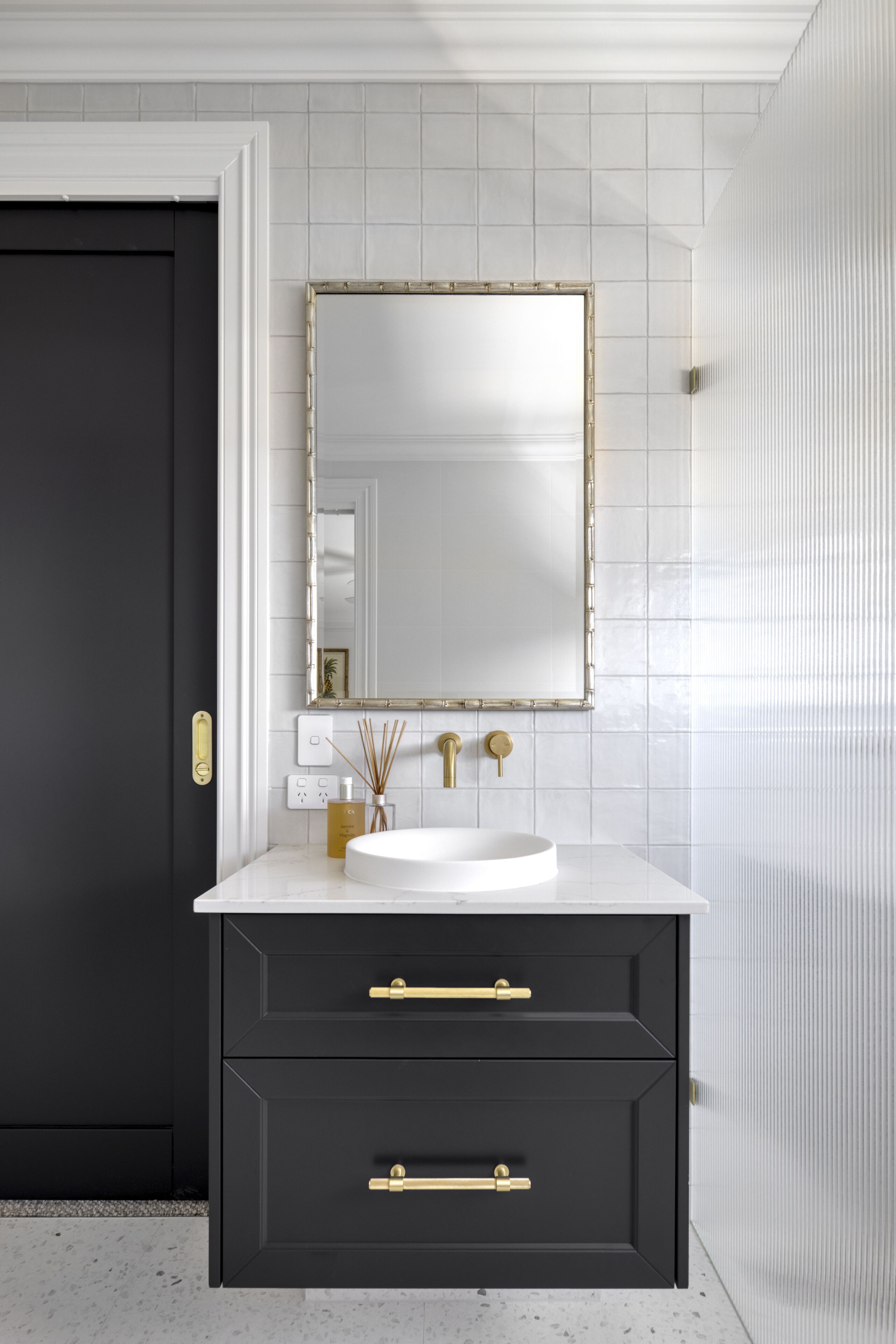 Une salle de bain avec un meuble-lavabo foncé, un lavabo blanc, des robinetteries dorées et un grand miroir.