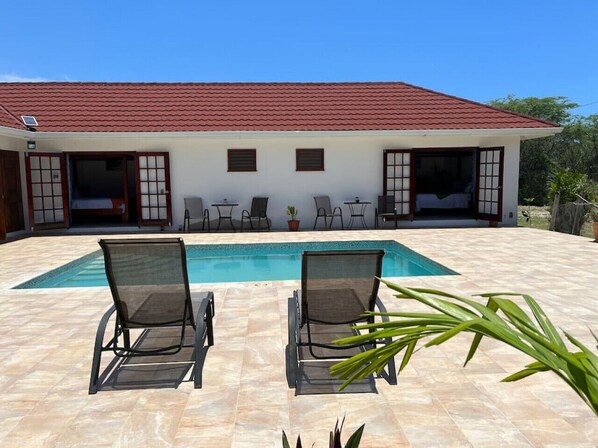 Uma casa com piscina, duas espreguiçadeiras e um pátio com azulejos.