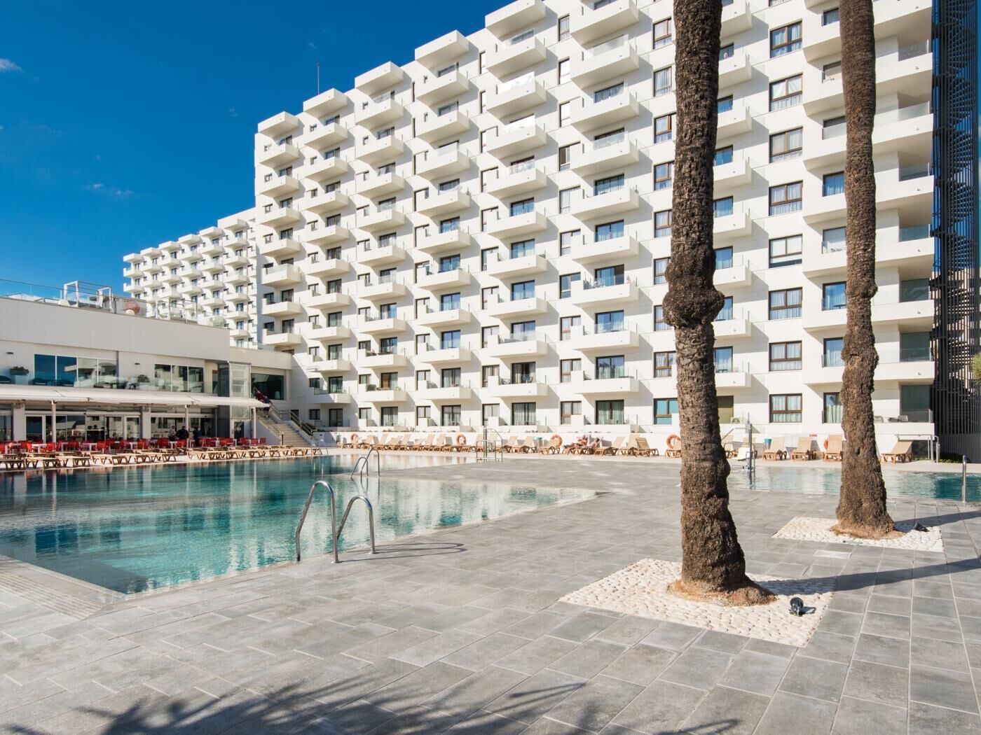 Ett hotell med ett stort poolområde, flera balkonger och en modern arkitektonisk design.