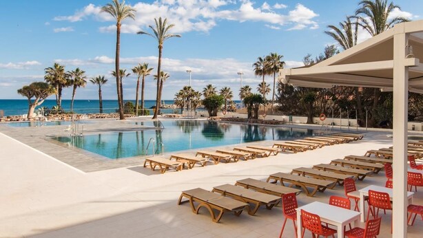 A poolside area with lounge chairs and tables, palm trees, and a view of the ocean. - Carihuela Beach Sun Private apartment (TORREMOLINOS)