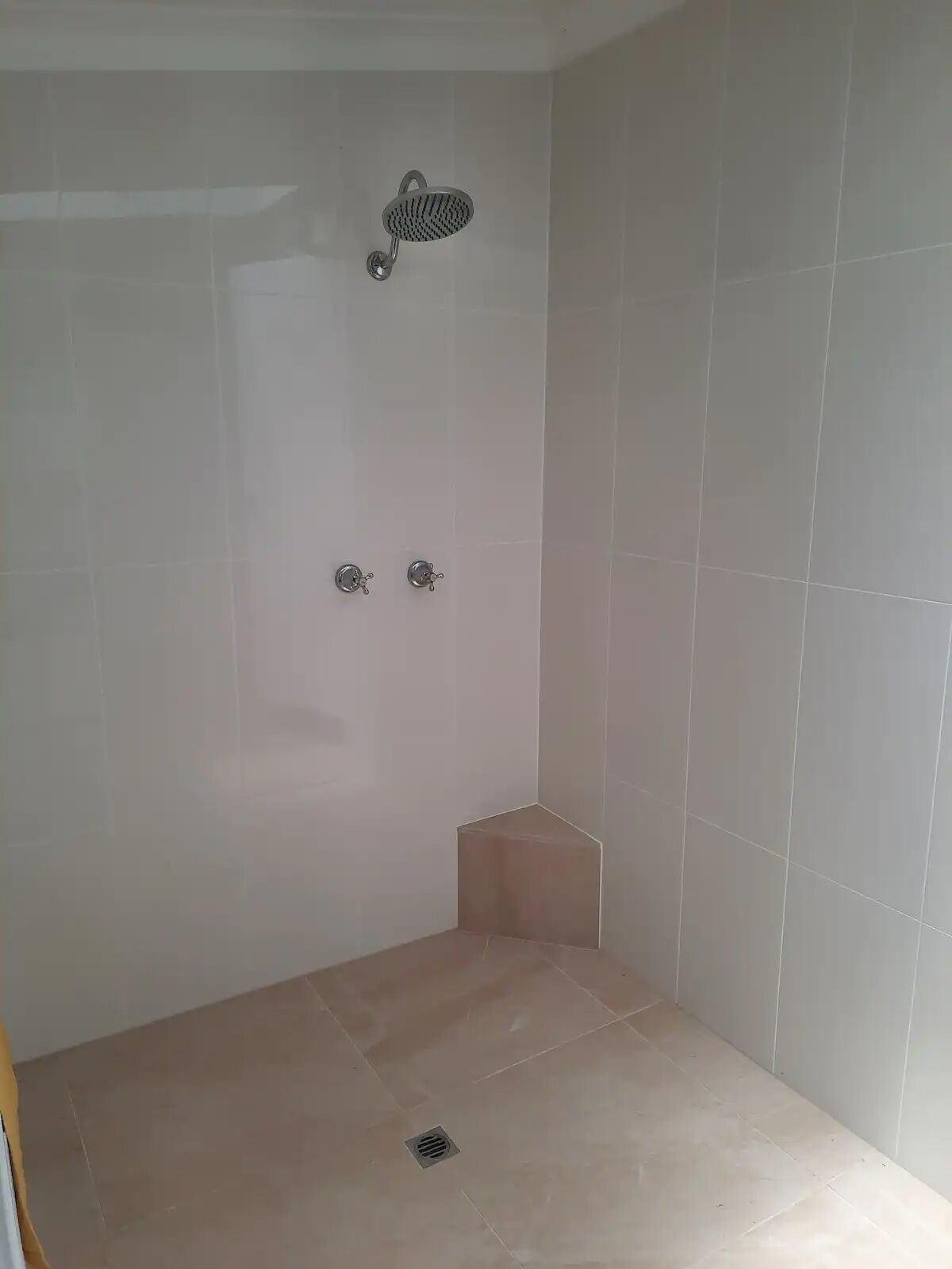Uma casa de banho pequena, revestida a azulejos, com um chuveiro e duas torneiras.
