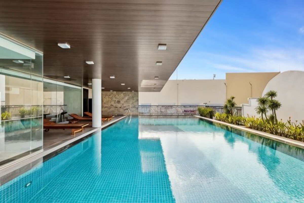 En modern inomhuspool med kristallklart blått vatten, omgiven av solstolar och en vägg av glas.