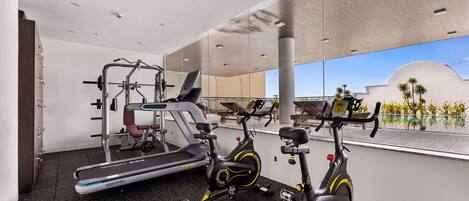 Un gimnasio con equipamiento de ejercicio, incluyendo una cinta de correr, bicicletas estáticas y una máquina de pesas.