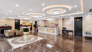 A hotel lobby with a marble floor, a reception desk, and a large decorative vase with flowers. - Florence Hotel (Da Nang)