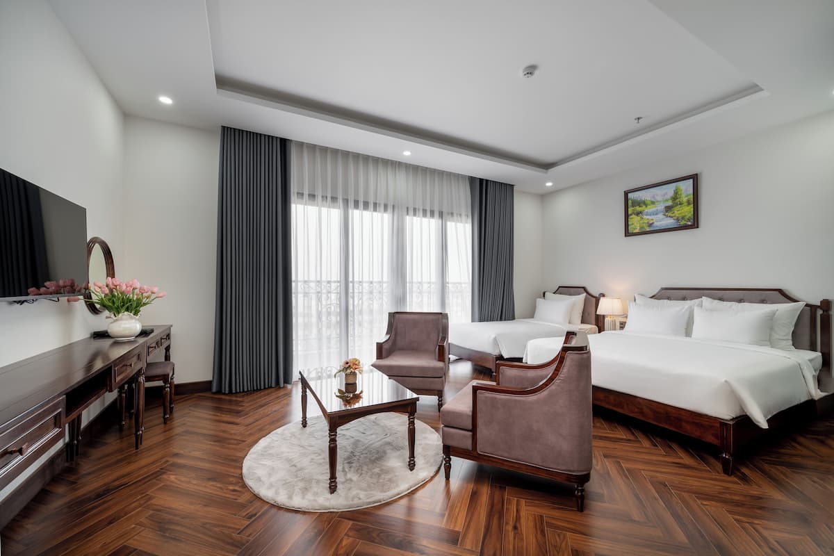 A hotel room with a bed, two armchairs, a desk, a TV, and a large window with curtains.