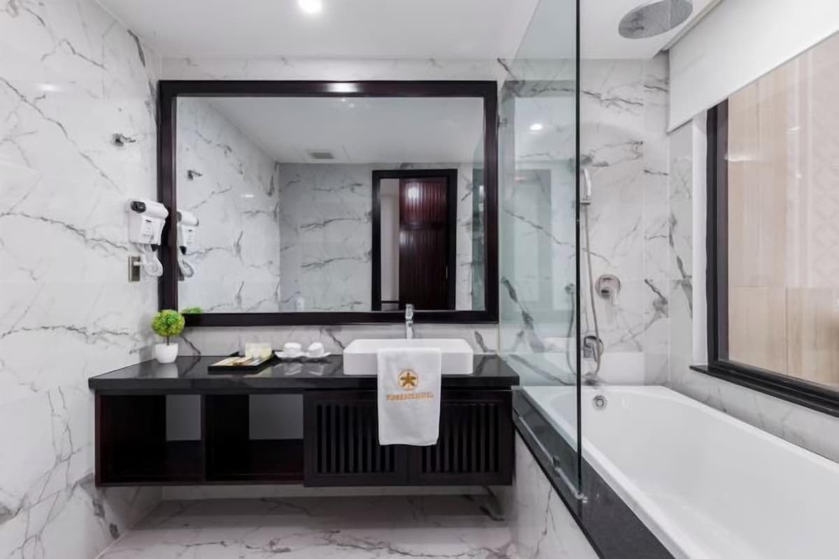 A modern bathroom with a marble wall, a large mirror, a black vanity, a white sink, a towel, and a bathtub.