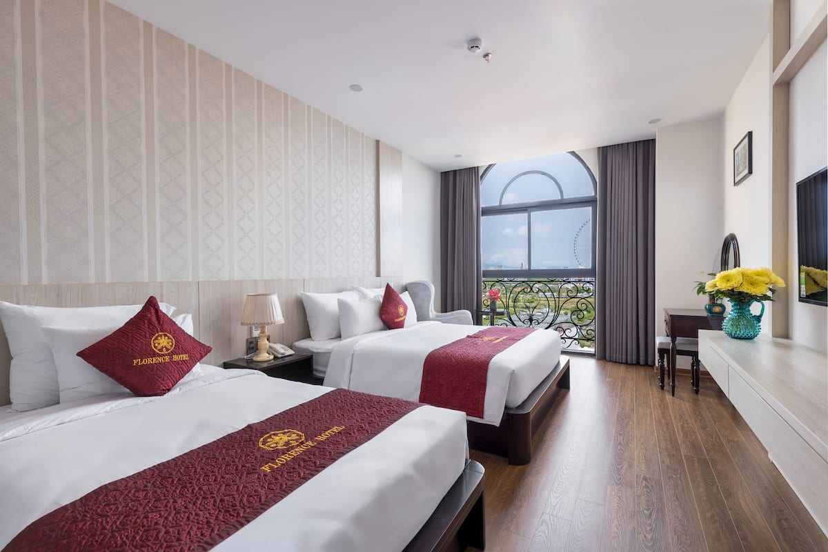 A hotel room with two beds, a balcony, a desk, and a TV.
