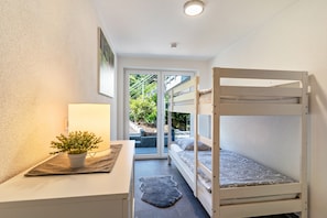 A bunk bed room with a desk, a potted plant, and a view through a glass door.