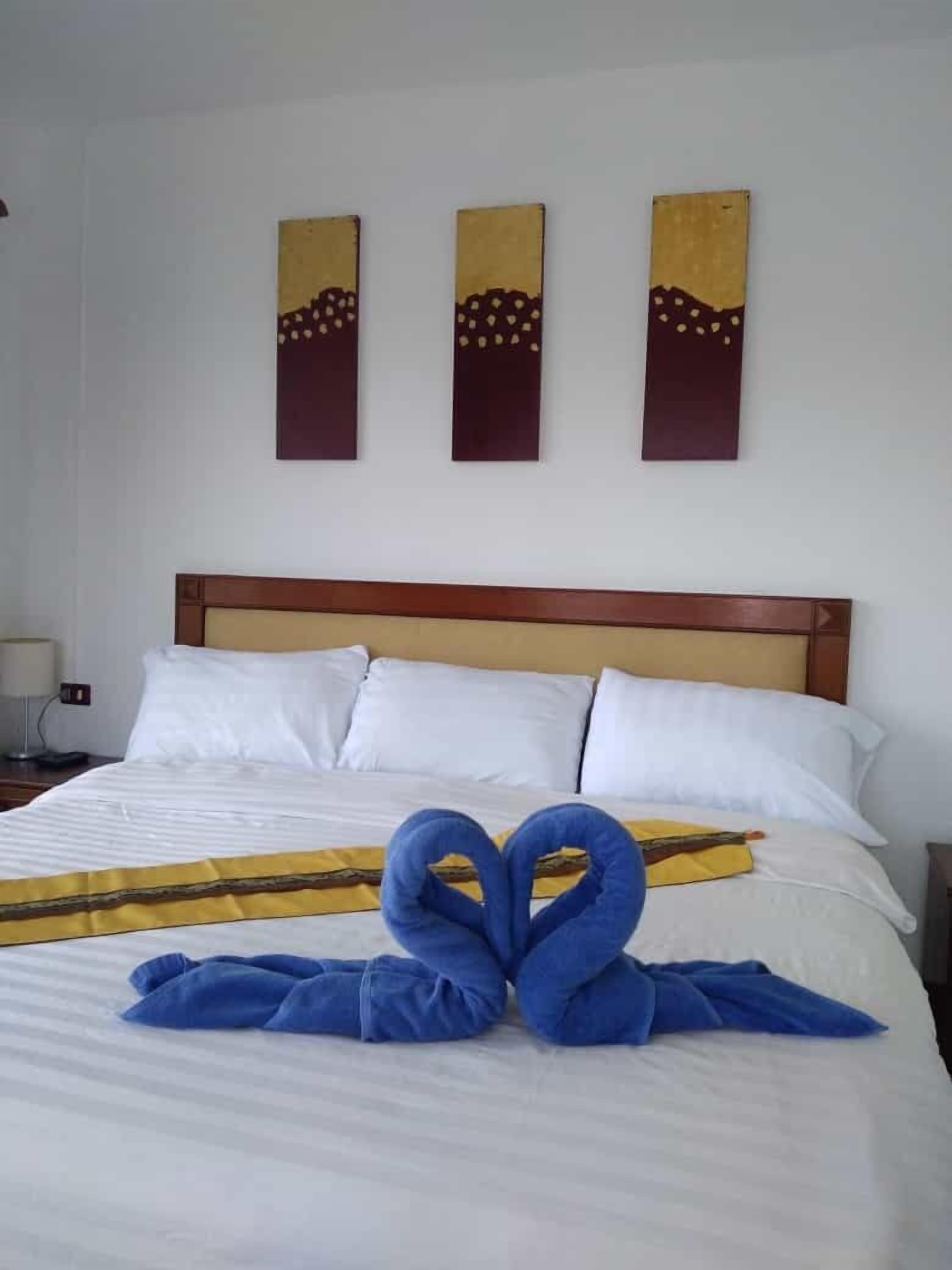 Une chambre d’hôtel avec un lit parfaitement fait, du linge de lit blanc et trois œuvres d’art accrochées au mur au-dessus de la tête de lit.
