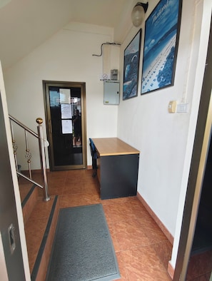 A hallway with a staircase, a desk, a chair, a door, and a poster on the wall. - Kamala Cool 2 (Kamala)