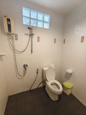 A bathroom with a toilet, a shower, a window, and a trash bin. - Kamala Cool 2 (Kamala)