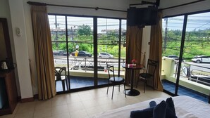 A hotel room with a large bed, a TV mounted on the wall, a balcony with a view of the street, and a small table with chairs. - Kamala Cool 2 (Kamala)