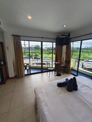 A hotel room with a large bed, a TV mounted on the wall, a balcony with a view of the street, and a small table with chairs. - Kamala Cool 2 (Kamala)